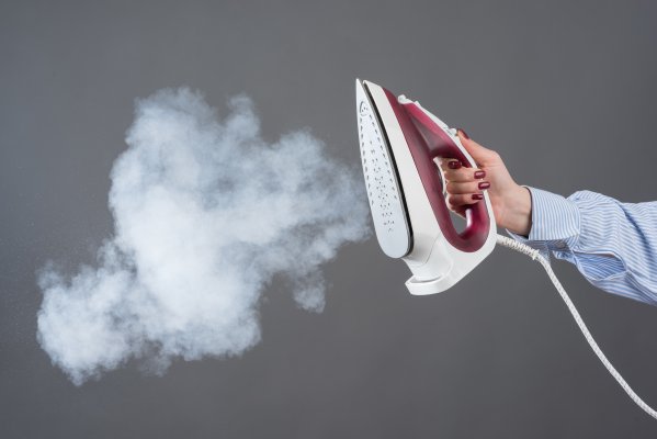 woman white shirt holding steam iron steam coming out gray background